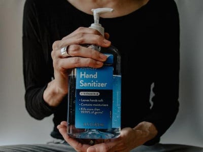 A large bottle of hand sanitizer being held in the centre of the image by a sitting adult.